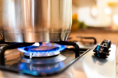 Closeup of gas stove top with blue fire flame knobs and stainless steel pot with reflection and bokeh blurry blurred background