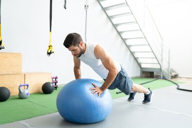 Active Man Doing Swiss Ball Push-Ups At Health Club