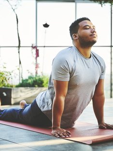 A strapping young black male doing Bhujangasana yoga pose in a studio