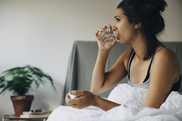 woman in bed drinking water to stop post-nasal drip