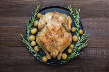 an overhead photo of a traditional roasted turkey with rosemary on a black platter on a wooden table