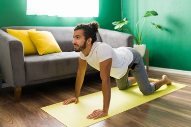 Person wearing white T-shirt and gray sweatpants doing cat-cow pose on yoga mat to reduce inflammation