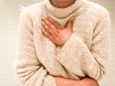 close view of a person wearing a beige sweater with their hand over their chest because they have shortness of breath from anxiety